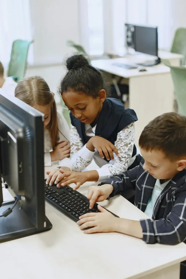 Children happily learning in a classroom, by collaborating together on a computer.